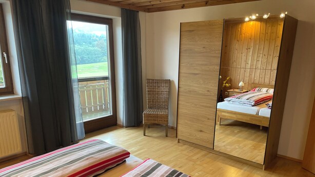 Een slaapkamer met een grote spiegel, een bed met streepjesbeddengoed, een stoel en uitzicht op een balkon.