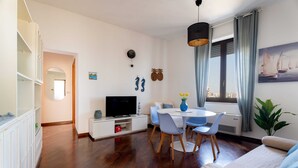 Ein modernes Wohnzimmer mit Essbereich, einem Flachbildfernseher und einem großen Fenster mit Vorhängen.