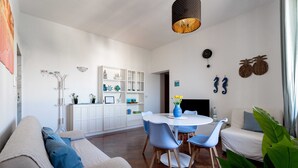 Ein modernes Wohnzimmer mit einer Couch, einem Esstisch, Stühlen und einer Küchenzeile im Hintergrund.