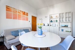 A modern living room with a round white table, blue chairs, a striped sofa, and a white cabinet with shelves. - Relax in riva by Monholiday (Monopoli)