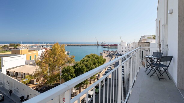 Ein Balkon mit Meerblick, ein Essbereich mit Stühlen und ein Gebäude mit weißer Fassade.