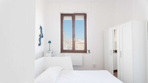Ein Schlafzimmer mit Bett, Kleiderschrank, Fenster mit Blick auf Gebäude und Wandradiator.