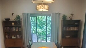 A dining room with a long wooden table, chairs, a central light fixture, and bookshelves with plants. - Welcoming 2-bedroom house with AC in charming San Simon (San Simon)