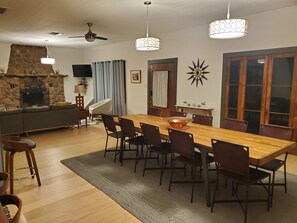 A dining area with a wooden table, chairs, a stone fireplace, and a television.