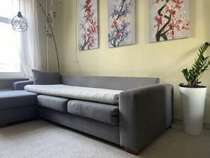 A modern living room with a grey sectional sofa, a potted plant, and three wall-mounted paintings. - Sunny Studio Apt with Free Parking (Rīga)