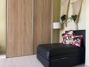 Ein Zimmer mit Schiebetürenschrank aus Holz, einer schwarzen Ledersofa, einem gemusterten Kissen, einer Stehlampe und Wandbehängen aus Makramee.