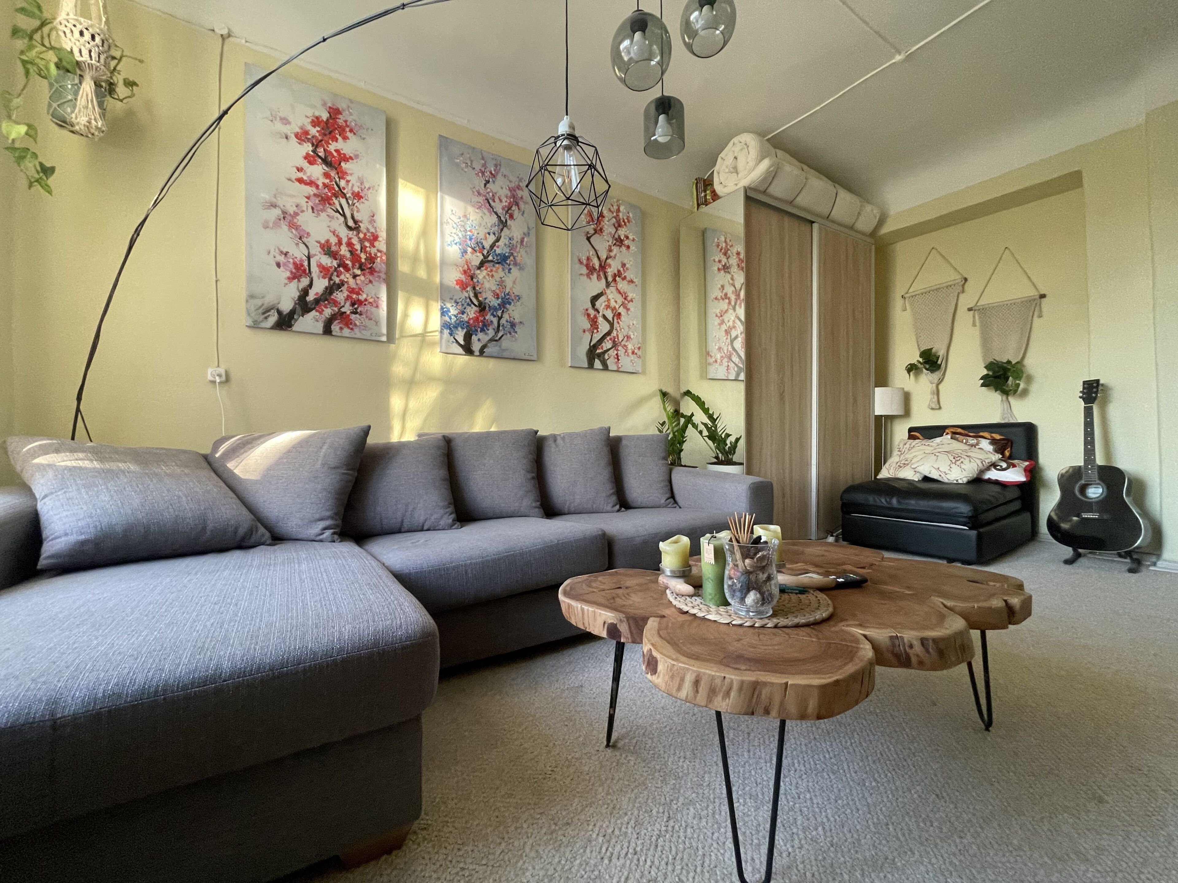 A living room with a grey sectional sofa, a wooden coffee table, and a black sofa with a guitar.