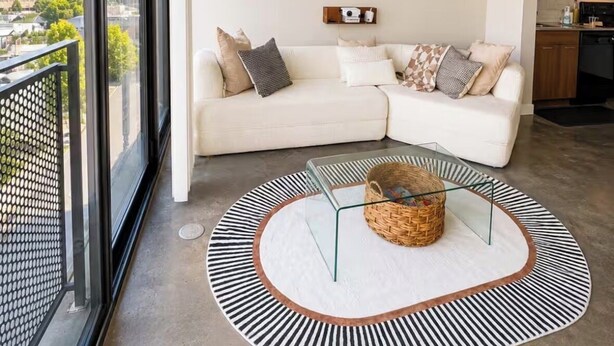 Een moderne woonkamer met een witte bank, een plafondventilator, uitzicht op de stad en een ronde salontafel met een mand.