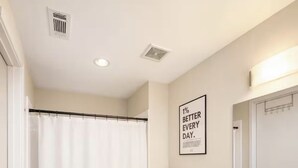 Een moderne badkamer met douchegordijn, toilet, wastafel en een motiverende quote op de muur.