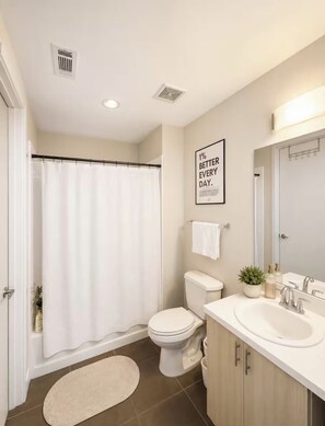 A modern bathroom with a shower curtain, toilet, sink, and a motivational quote on the wall. - Modern Midtown Condo (Atlanta)