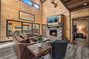 A cozy cabin interior with a stone fireplace, wooden walls, and a mounted deer head. - Bluff Ridge Retreat + SwimSpa + Hot Tub+ Air Hockey + (Sevierville)