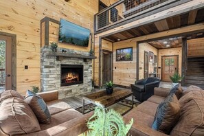 A log cabin interior with a stone fireplace, leather sofas, and a TV mounted on the wall. - Bluff Ridge Retreat + SwimSpa + Hot Tub+ Air Hockey + (Sevierville)