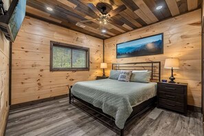 Ein Schlafzimmer mit Holzwänden, einem Bett, zwei Nachttischen, einem Deckenventilator und einem Fenster mit Jalousien.