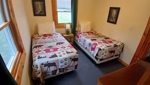 Ein Zimmer mit zwei Betten, einem Fenster, einer Lampe und einem Bild an der Wand.