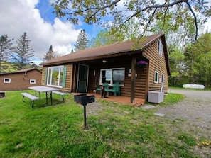 A log cabin with a porch, a picnic table, and a green chair outside.