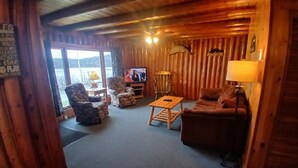Interior acollidor d'una cabana, amb elements de fusta, televisió, sofà, cadira i taula petita.