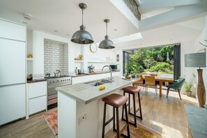 Eine moderne Küche mit einer zentralen Kochinsel, Barhocker und einem Essbereich mit Gartenblick.