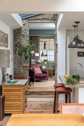 Ein gemütliches Interieur mit einer Steinwand, einem Holzespeisetisch, einem violetten Stuhl und einer Küchenzeile mit Spüle und Pendelleuchte.
