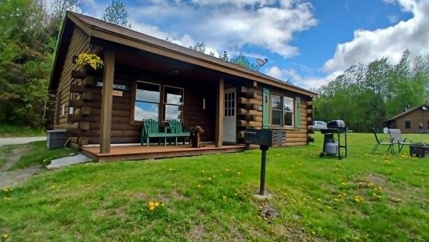 Une cabane en rondins avec un porche, des chaises vertes et une boîte aux lettres.