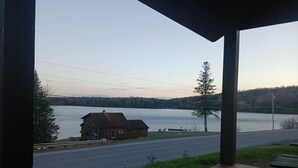 Um deck de madeira com vista para um lago, uma cabana pequena e uma estrada.