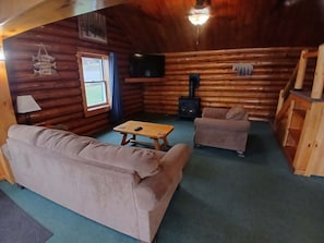 A log cabin interior with a sofa, armchair, and a small table. - Lakeview 5 — 1st Lake Waterfront 4 Bedrooms • Sleeps 9 • Dock • Direct Snowmobile Trail Access (Pittsburg)
