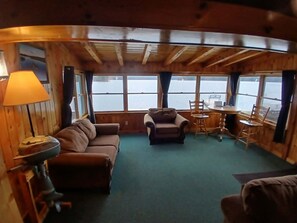 A cabin interior with a sofa, armchair, dining table, and chairs. - Lakeview 5 — 1st Lake Waterfront 4 Bedrooms • Sleeps 9 • Dock • Direct Snowmobile Trail Access (Pittsburg)