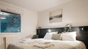 A bedroom with a bed, a window, a radiator, and a hanging light fixture. - Les Loges Du Leman (Crozet)