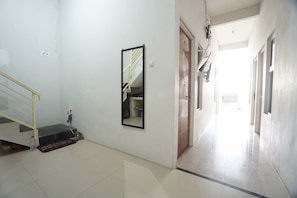 A hallway with a staircase, a mirror, and a door leading to another room.