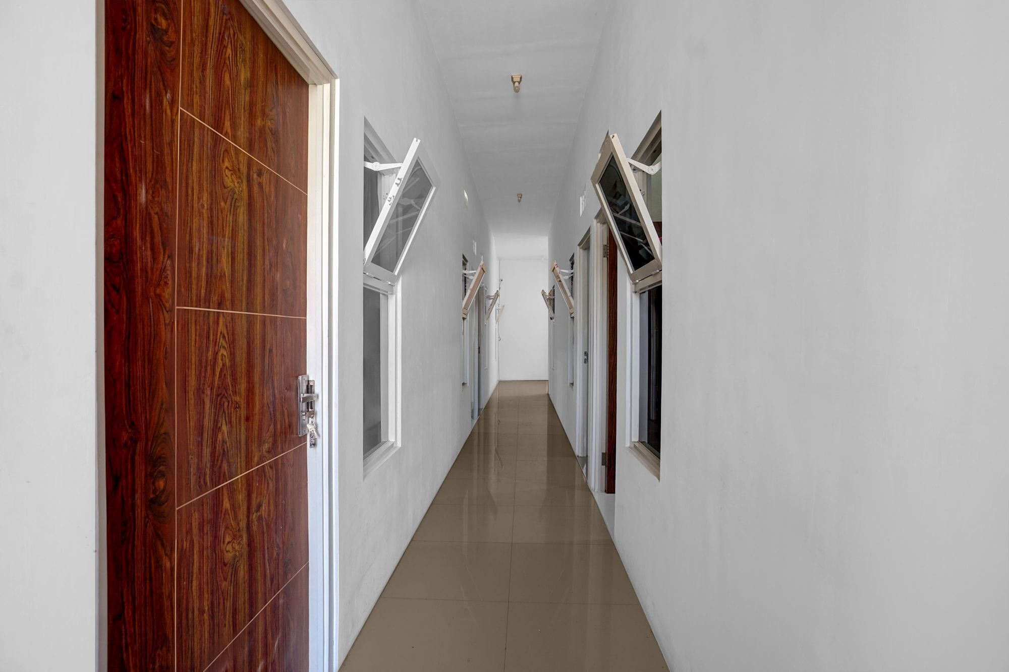 A corridor with white walls, wooden doors, and windows with blinds.
