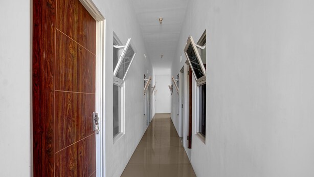Um corredor com paredes brancas, portas de madeira e janelas com persianas.