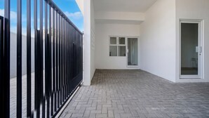 Um corredor com grade de metal preta, uma porta com janela e piso de azulejos.