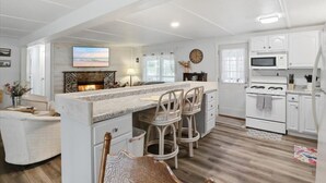 A modern kitchen with a central island, white cabinetry, a microwave, stove, and a television above the island. - Lake Ozark Getaway With Fire Pit & Flat Lot (Lake Ozark)