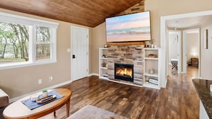 A living room with a fireplace, wooden floors, a television, and a view of the outdoors. - Perfect Lake Escape Near Bagnell Dam Strip (Lake Ozark)