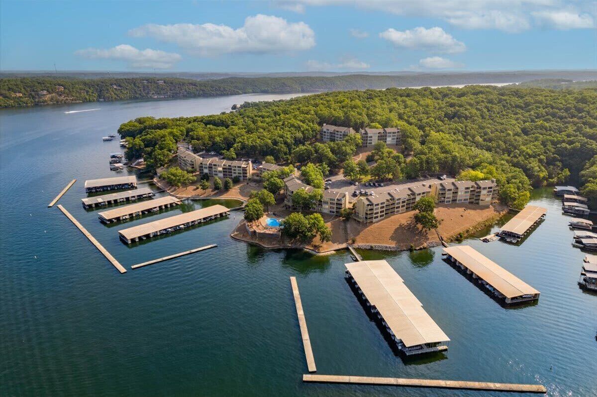 An aerial view of a lakeside hotel with docked boats, a swimming pool, and lush greenery.