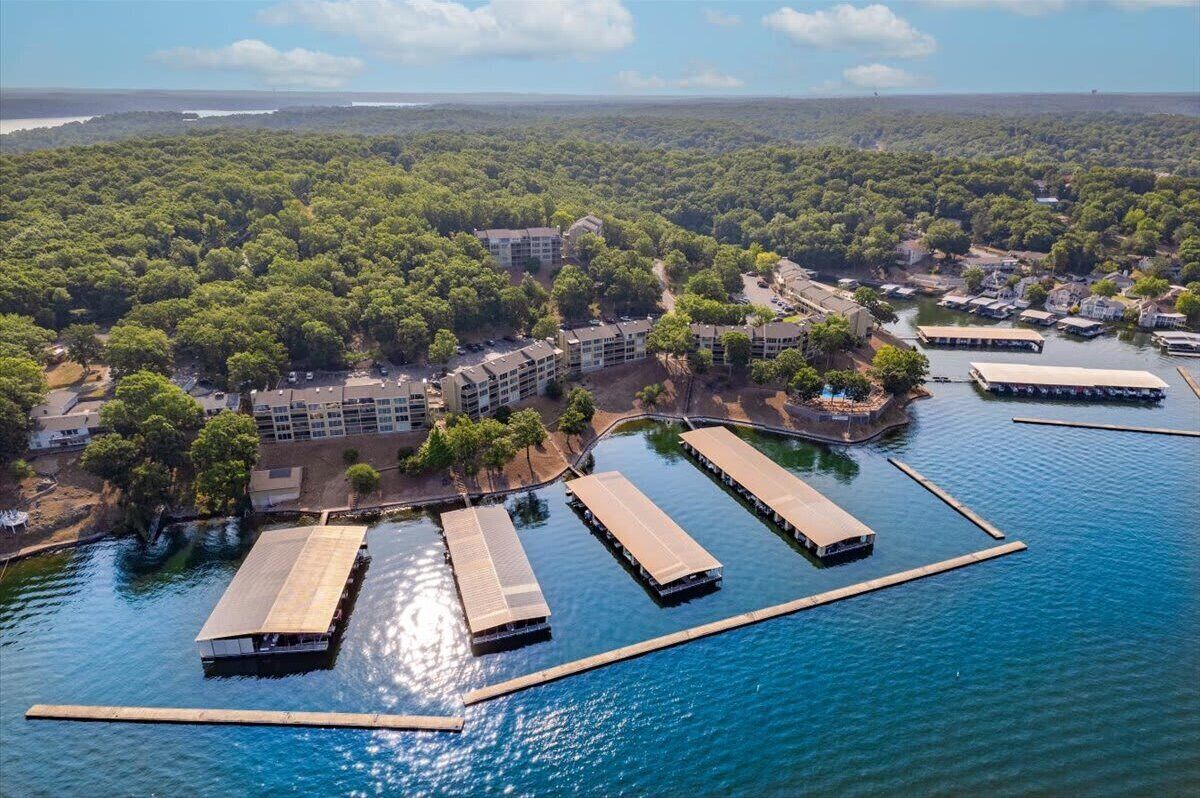 An aerial view of a waterfront property with multiple dock structures, a dense forested area, and a large building complex.