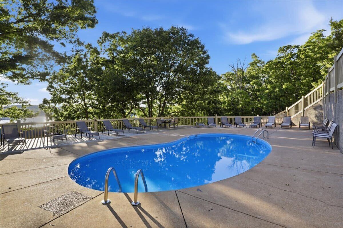 En swimmingpool med liggestole og en terrasse, omgivet af træer.
