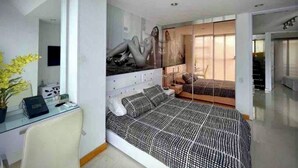 A modern bedroom with a large bed, a desk with a chair, a mirror, and a sliding door leading to another room. - DUPLEX ROOF CHAPINERO ALTO (Bogotá)