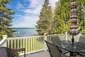 A deck with a table and chairs, overlooking a body of water and trees.
