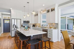 A modern kitchen with white cabinets, a large island, bar stools, and pendant lighting.