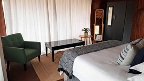 Una habitación con una cama, un sillón verde, una mesita, un espejo y un armario.