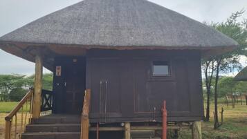 Una construcción con techo de paja, una pequeña ventana, escalones de madera y una puerta.