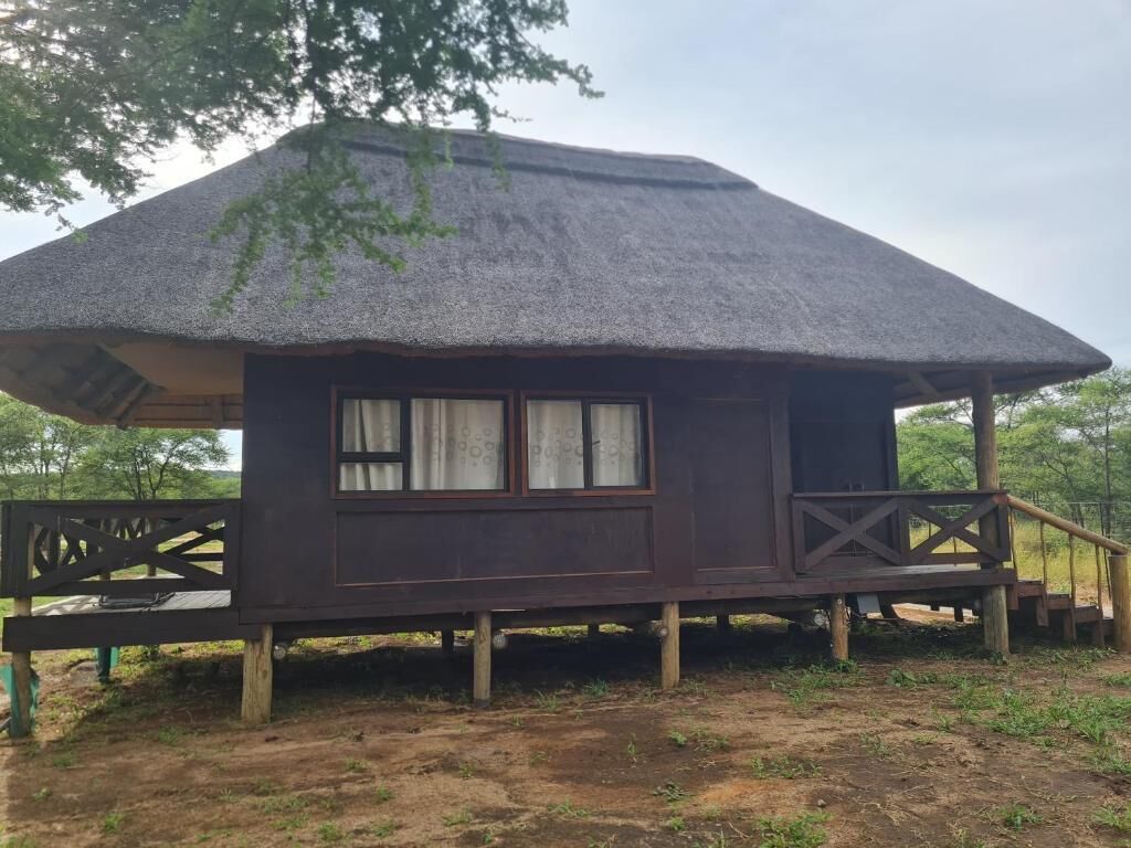 Una cabaña con techo de paja, una terraza de madera y ventanas.