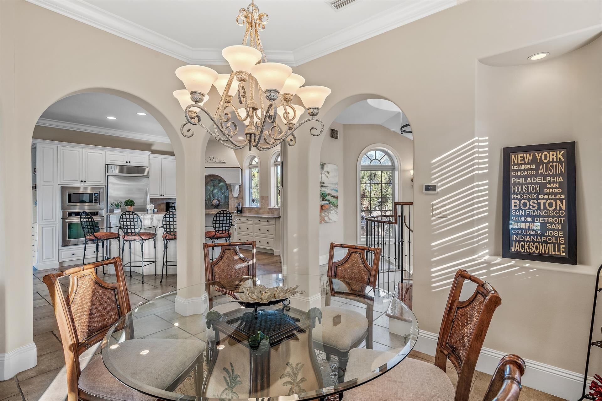 A dining area with a glass table surrounded by chairs, a chandelier, and a view of the kitchen.