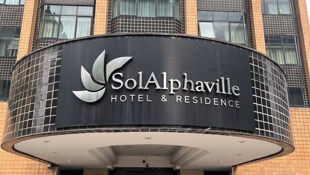 L’entrée d’un hôtel, avec une façade incurvée, une enseigne indiquant « SolAlphaville Hotel & Residence », et une entrée fermée par un portail.