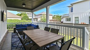 Eine überdachte Terrasse mit Holztisch und -stühlen, einem blauen Sofa und einem weißen Zaun.