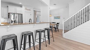Eine Küche mit weißen Schränken, einem Edelstahlkühlschrank und einer Bar mit Hockern.