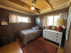 A bedroom with a bed, dresser, window with curtains, ceiling fan, and a rug. - 3-bedroom house in delightful Manistee with AC for comfort (Manistee)