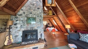 Ein gemütliches Schlafzimmer im Dachgeschoss mit Kamin aus Stein, Holzbalken, einem Esstisch mit Stühlen und einer Couch.