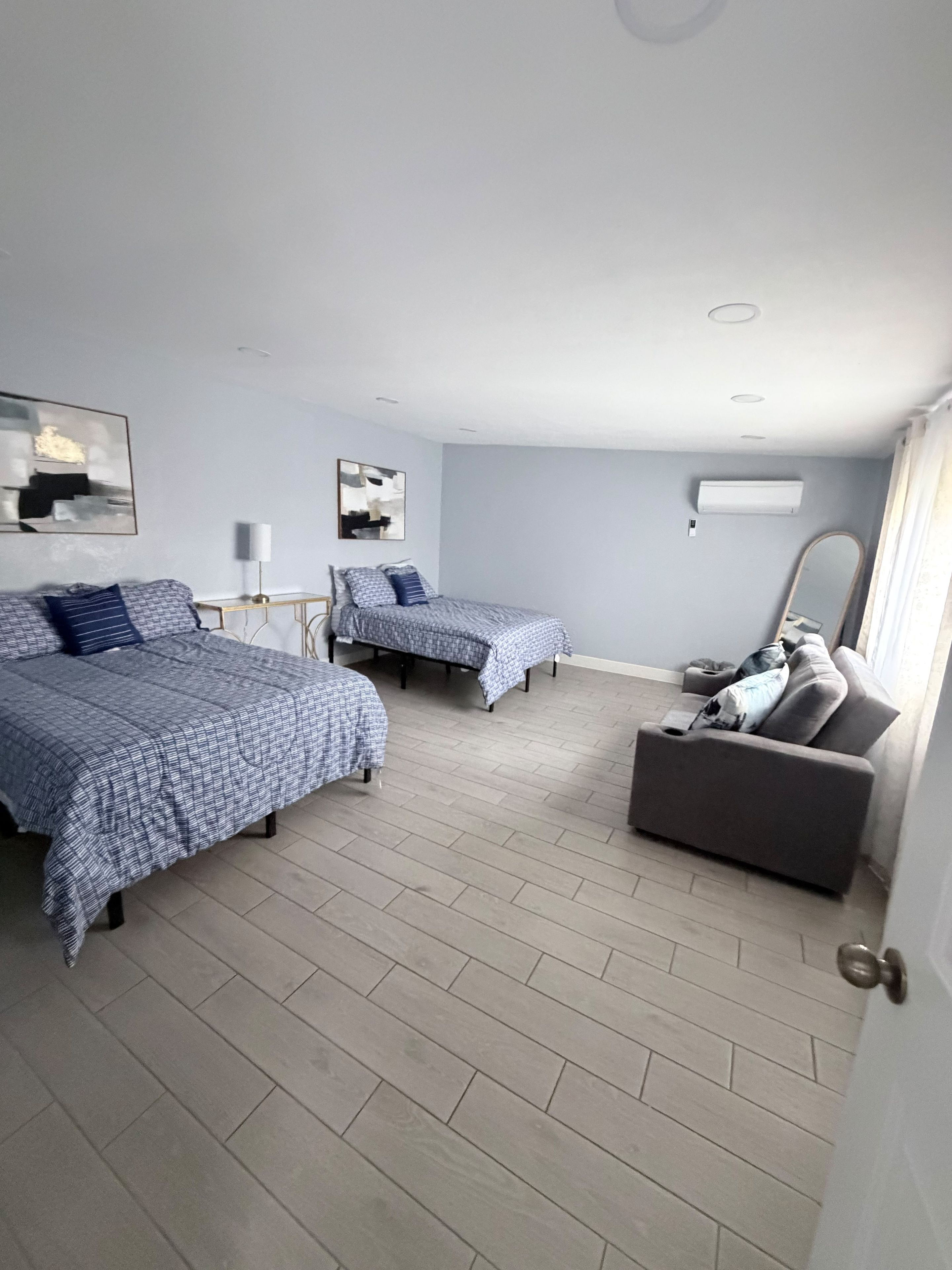A hotel room with two beds, a sofa, a lamp, and a mirror.