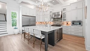 Uma cozinha moderna com armários brancos, uma ilha central, eletrodomésticos de aço inoxidável e um lustre.